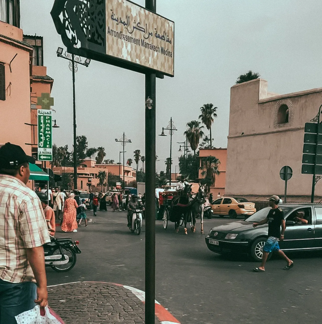 A very busy road in Marrakech with pedestrians, motorbikes, cars, and horses