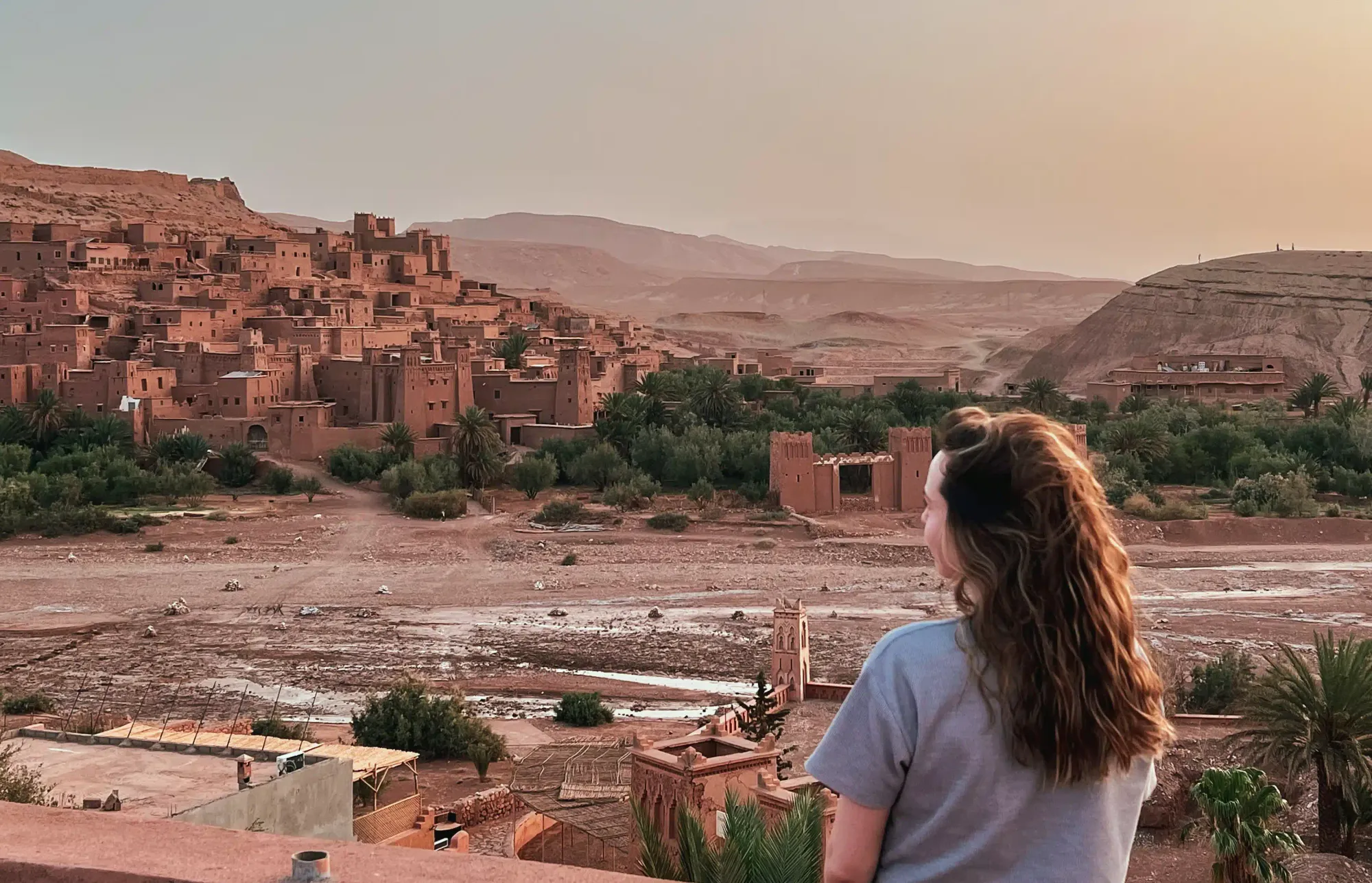 Girl standing on a balcony overlooking Ait Ben Haddou at sunrise.