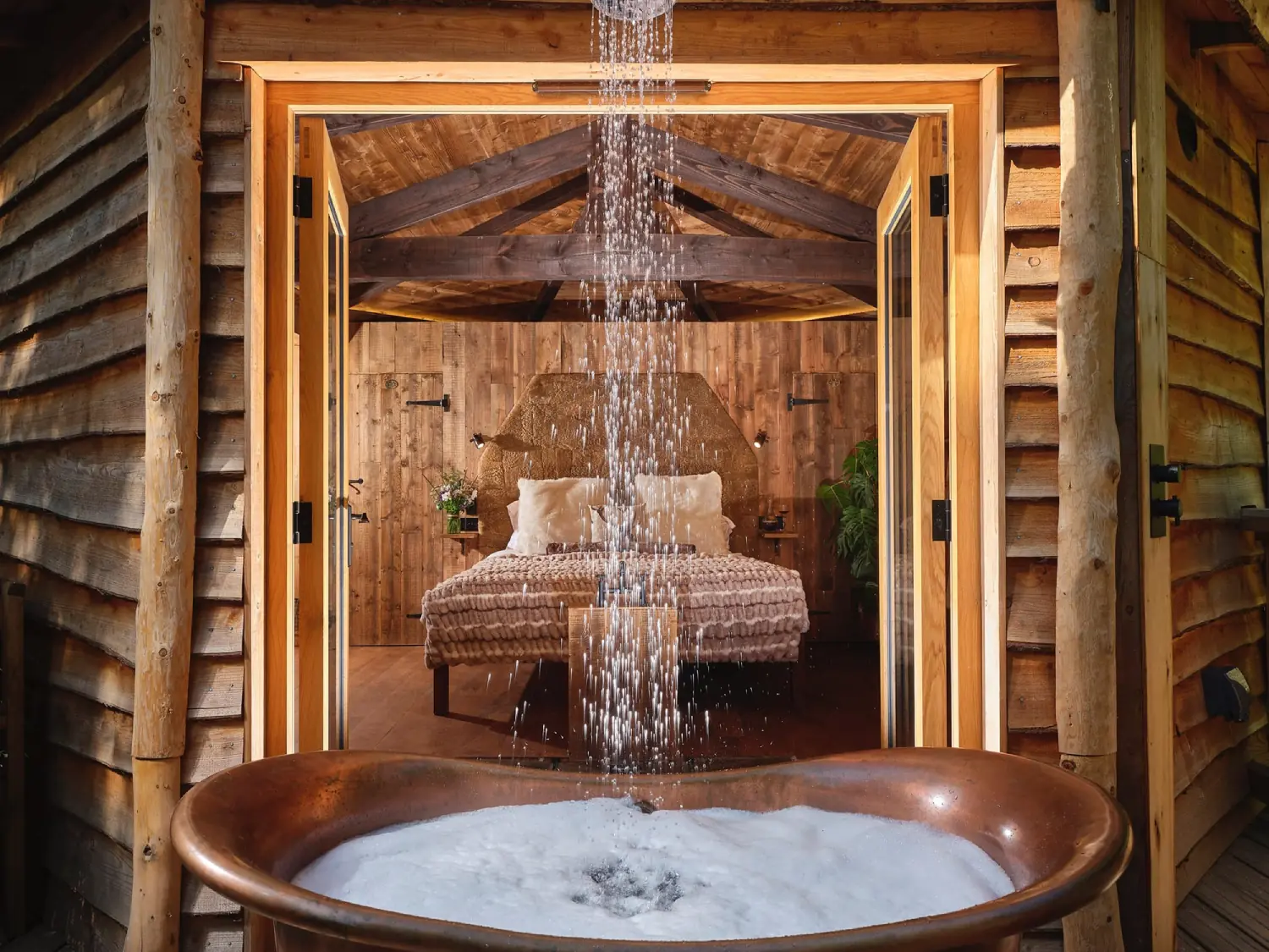 Outdoor bath with bed in the background at Hideout Treehouse, Sleepy Owl Retreats Devon.