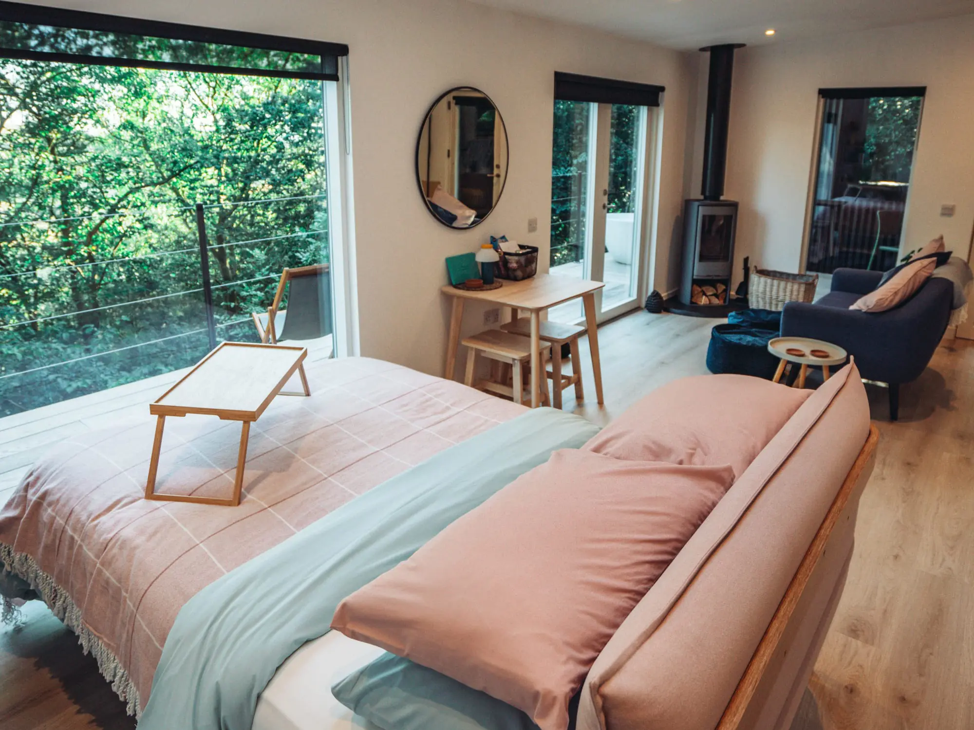 Inside of Bracken Treehouse with double bed facing out to the trees and living room with wood burner.