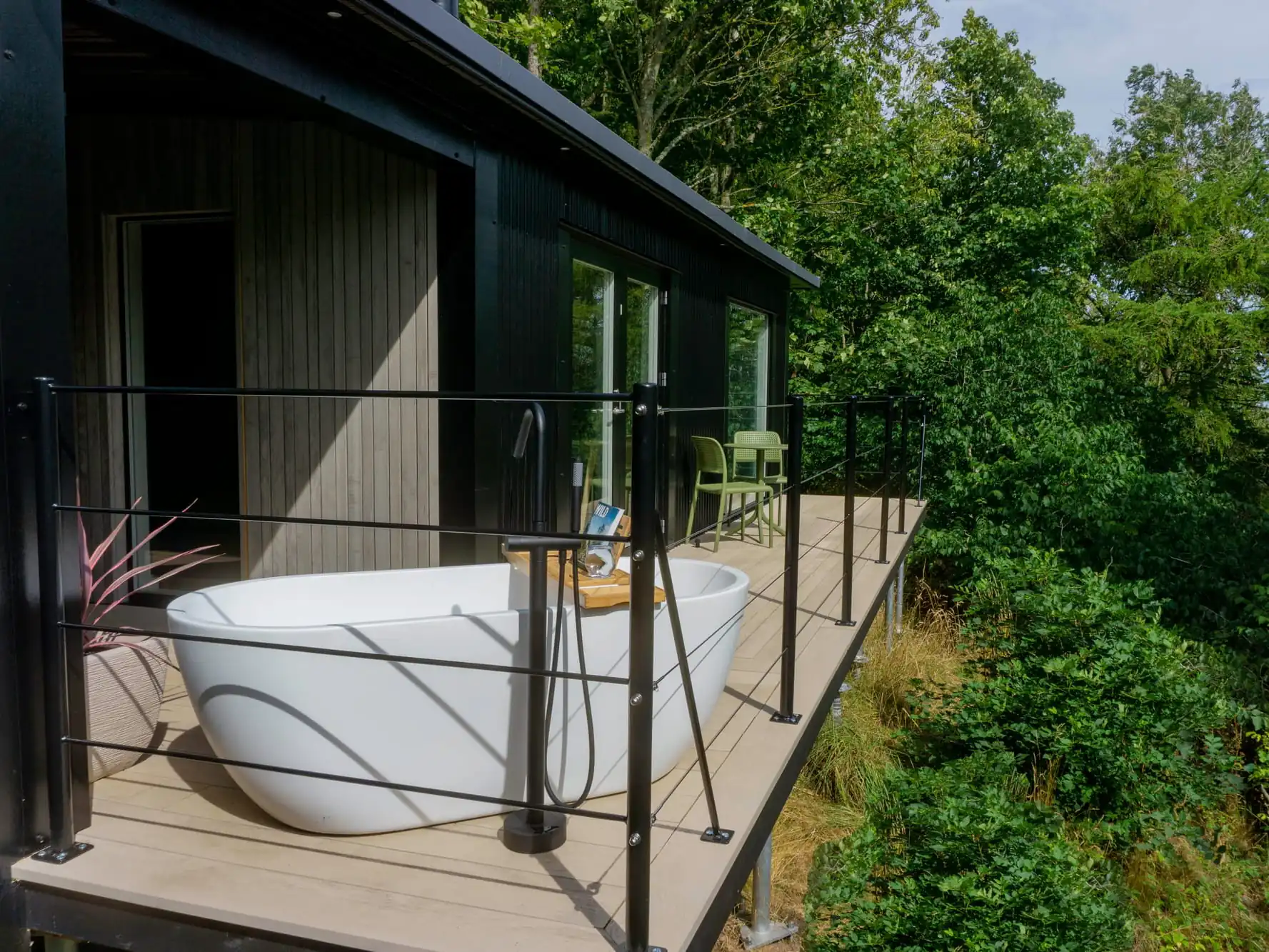 The outside of Bracken Treehouse: with decking, outdoor soaking tub, seating area, and tree canopy.