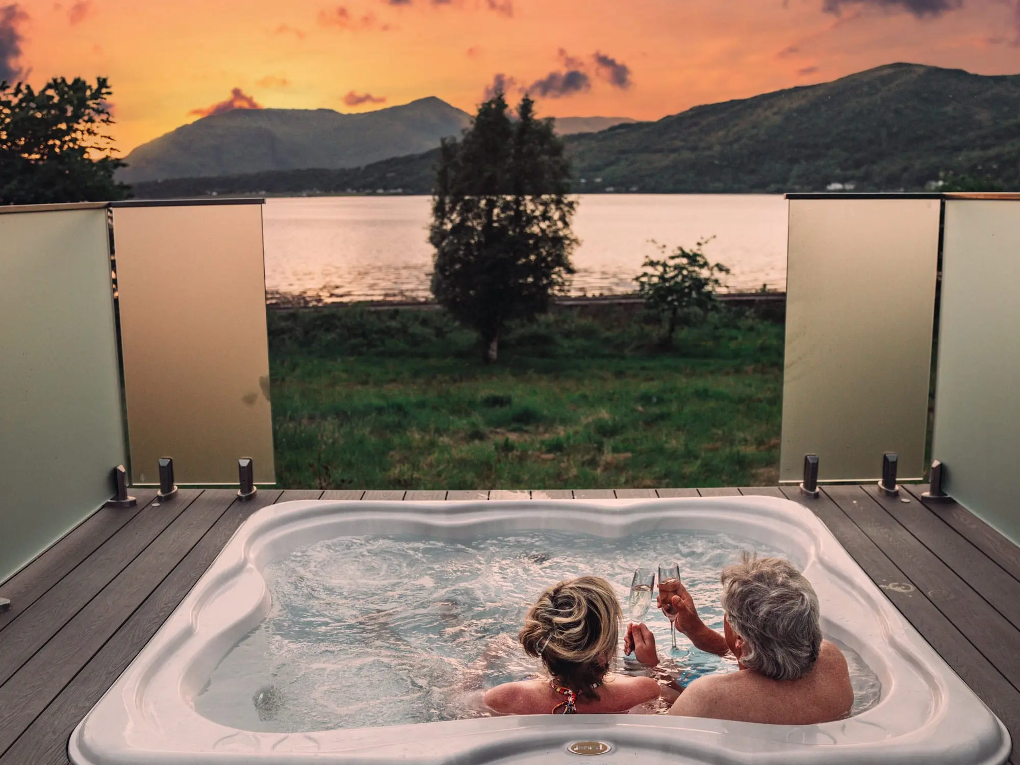 Couple in the sunken hot tub at Seabed Luxury Lodge overlooking the surrounding loch and hills.