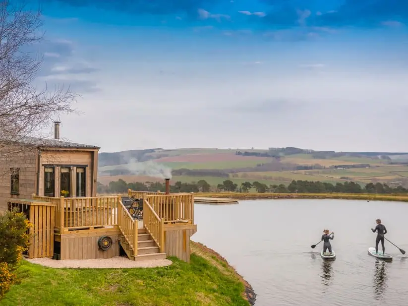 A couple paddleboarding on the loch surrounding the Tiny Homes lodge.