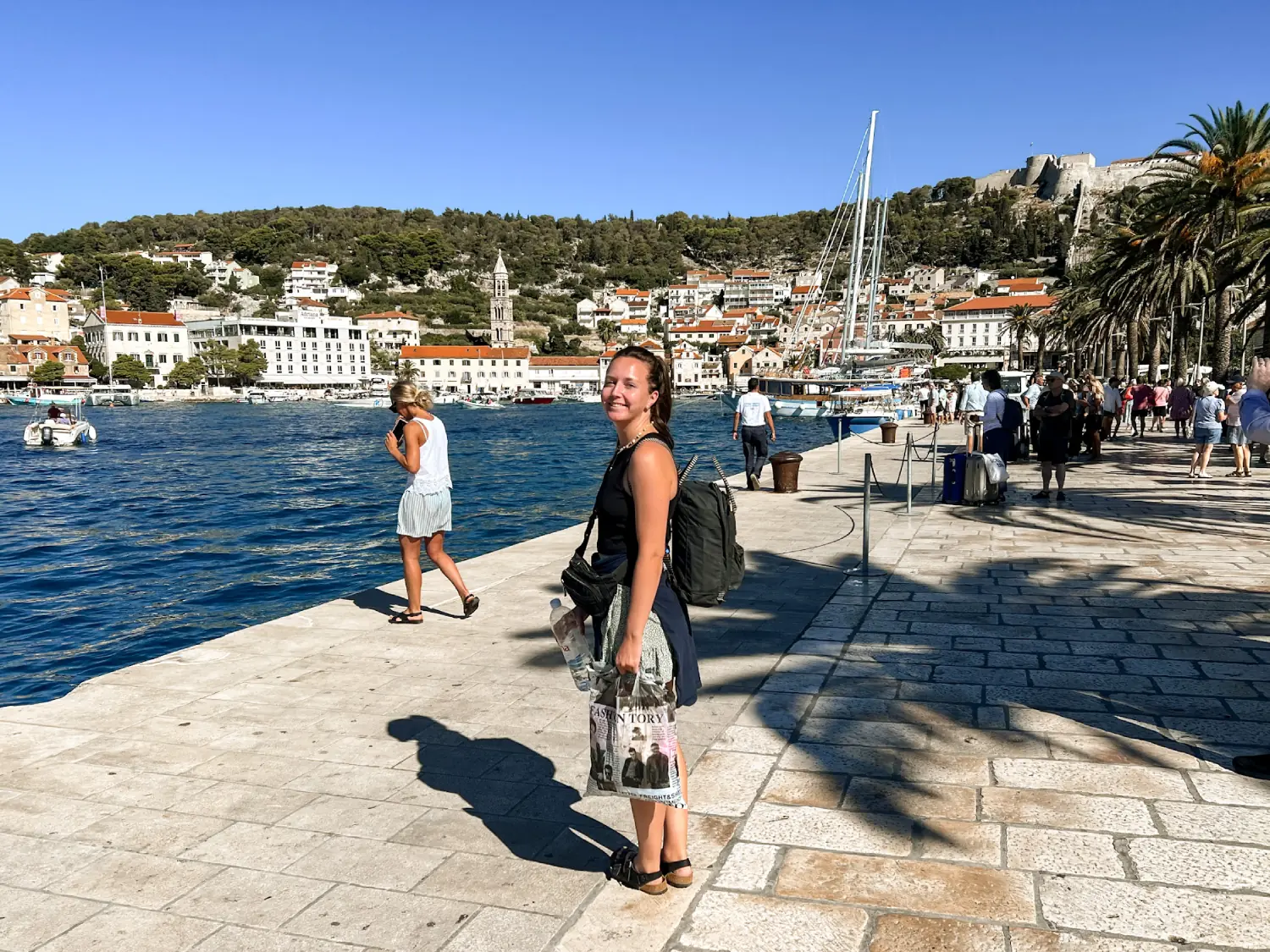 Girl standing in sunny Hvar Old Town Promenade waiting for a boat. 