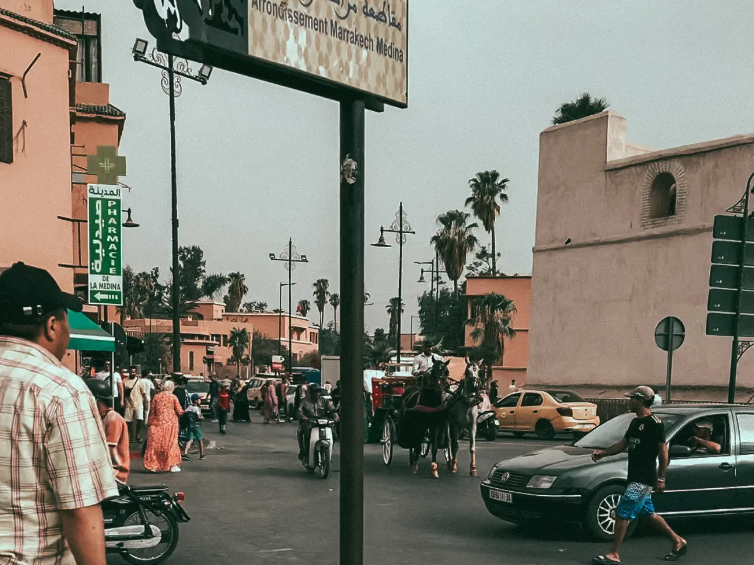 A very busy road in Marrakech with pedestrians, motorbikes, cars, and horses